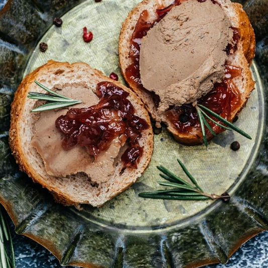 Two slices of bread with pate and jam on a rustic metal plate.