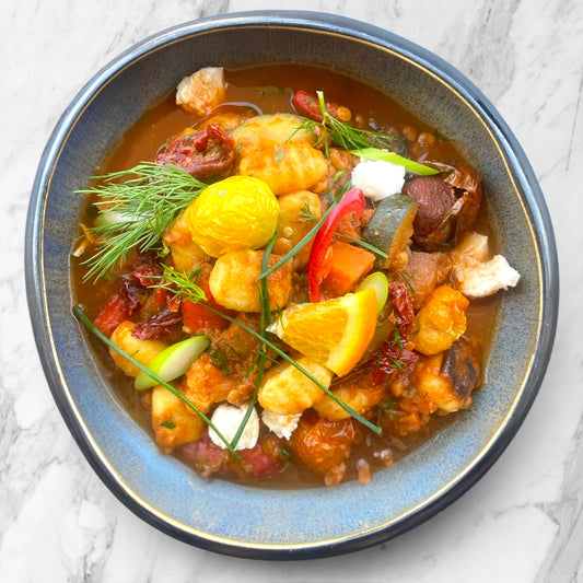  bowl of colorful vegetable stew with gnocchi on a marble surface