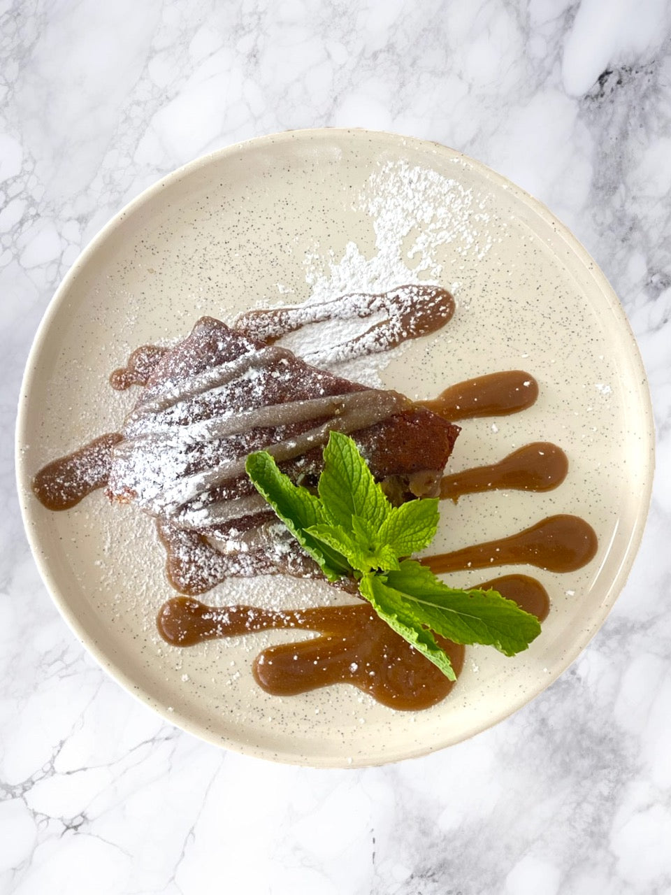 Dessert plate with chocolate pastry, mint leaves, and caramel sauce on a marble background