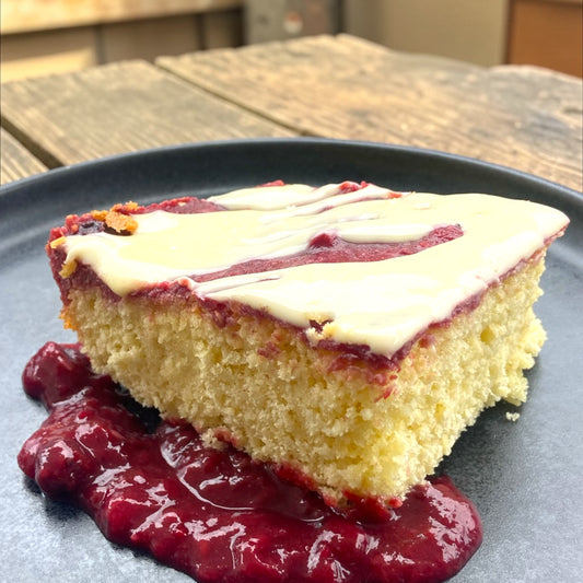 Slice of cake with white frosting and red fruit sauce on a dark plate.